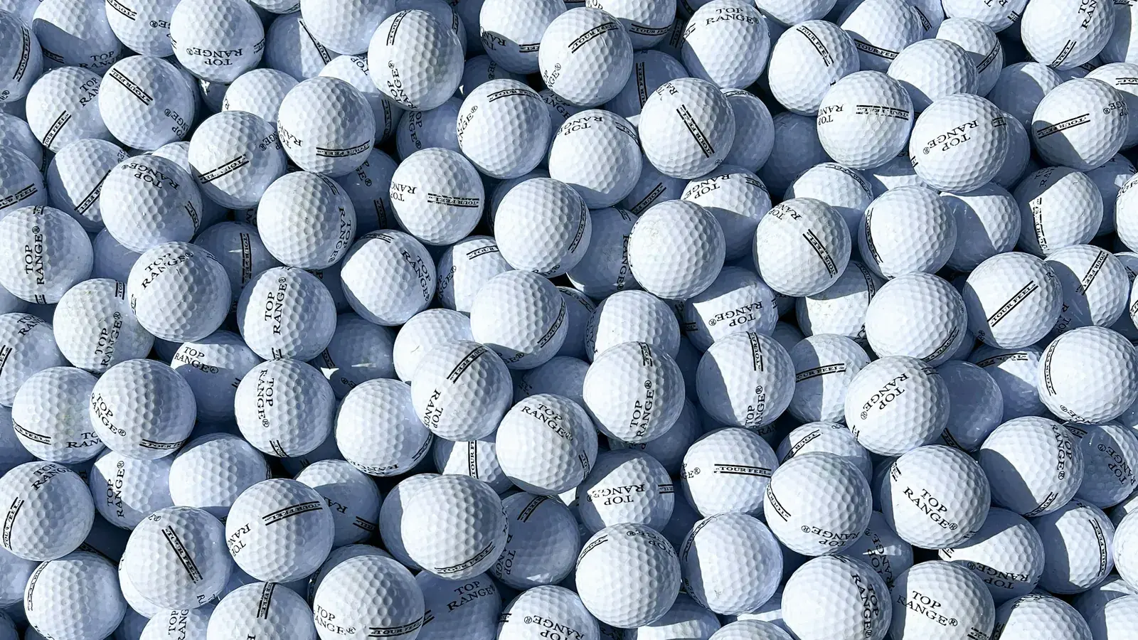 A dense pile of white driving-range golf balls printed "Top Range", lit by low sunlight