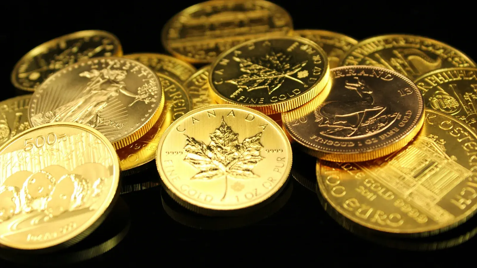 A loose pile of one-ounce bullion coins — Canadian Maple Leaf, Krugerrand, Austrian Philharmonic and American Eagle among them