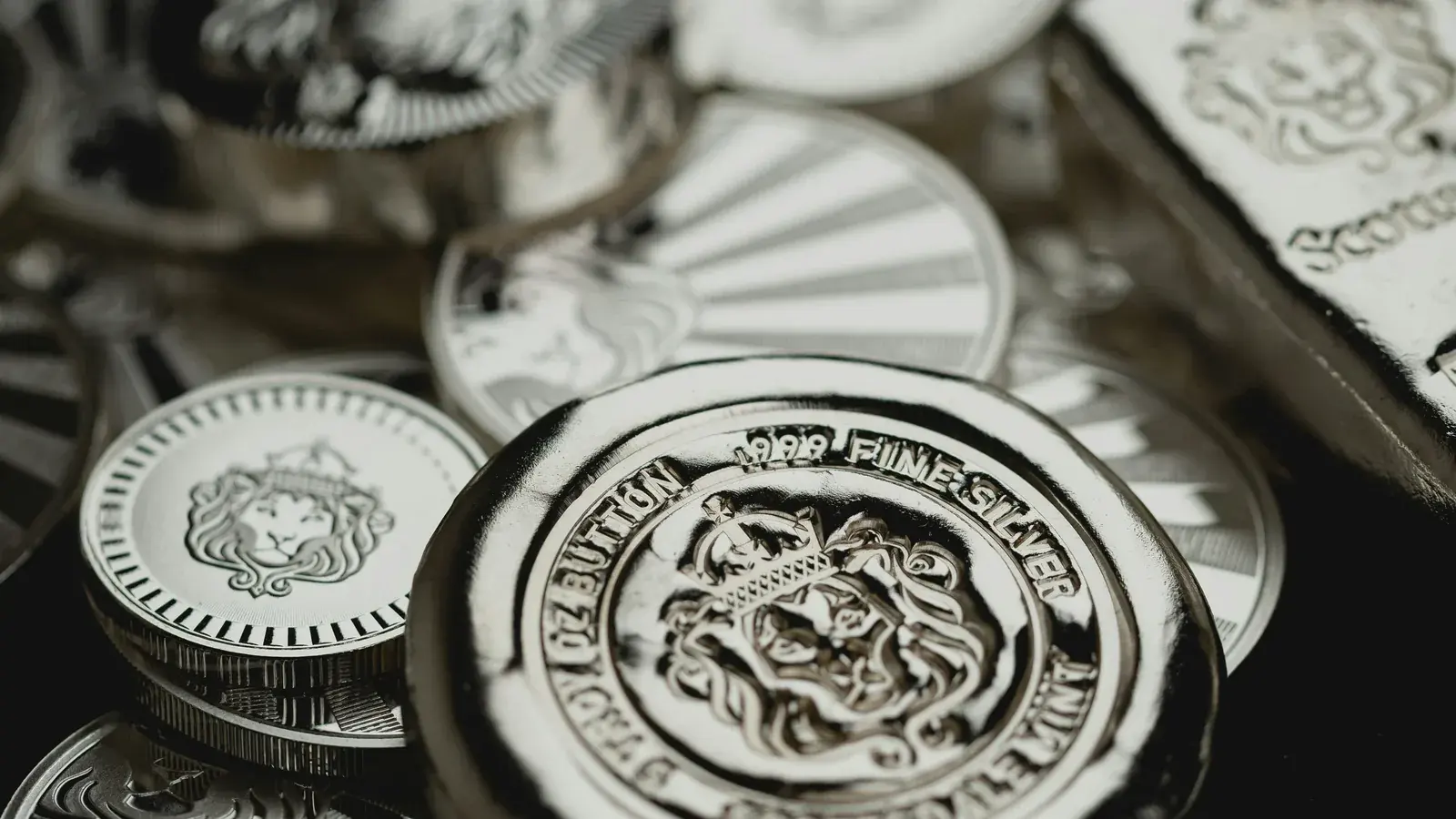 Silver rounds and a bar in close-up, the nearest coin reading 999 fine silver around a crowned lion.