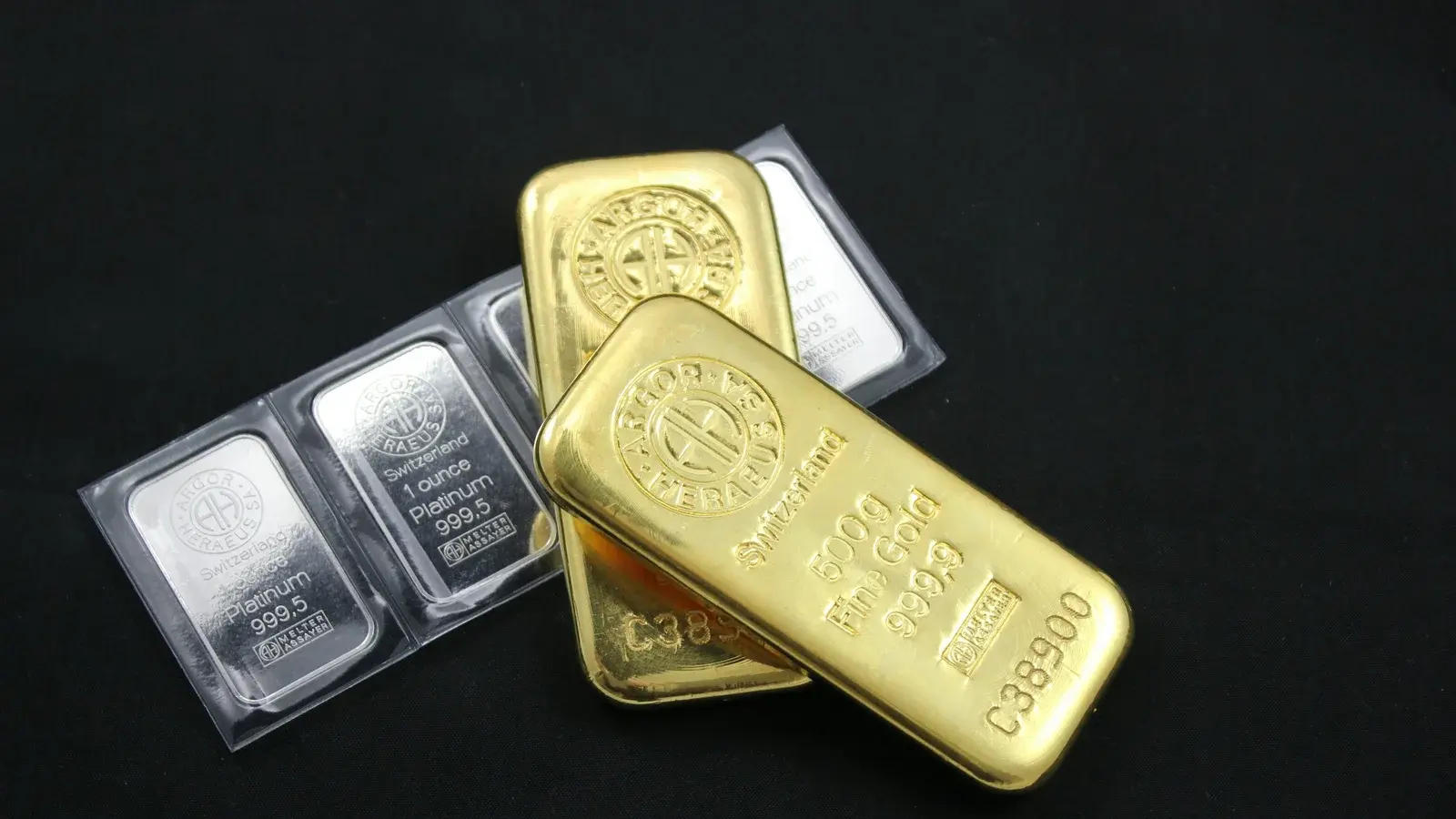 Two poured gold bars resting across sealed one-ounce silver bullion bars on a black surface
