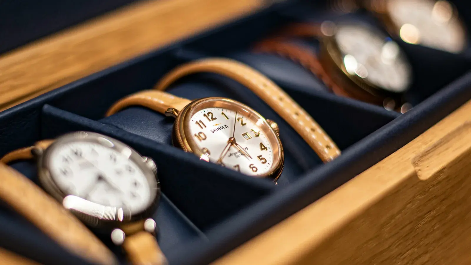 Wristwatches lying in the navy velvet trays of an open oak watch box.