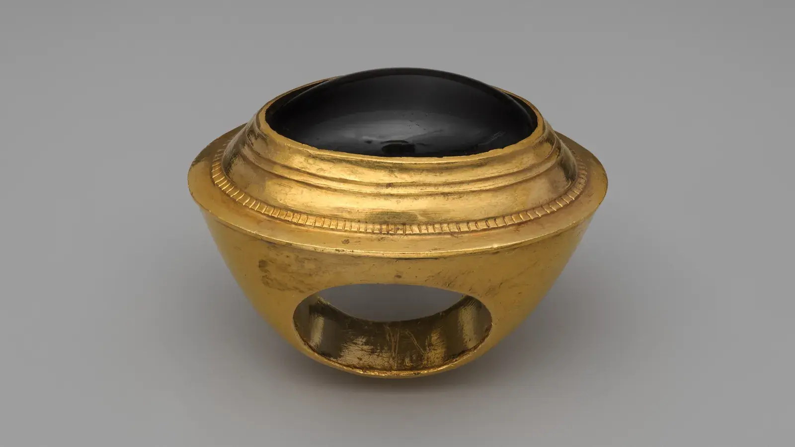 A gold ring of the 3rd or 2nd century BCE set with a domed dark garnet, seen from the side so the band and finger opening show